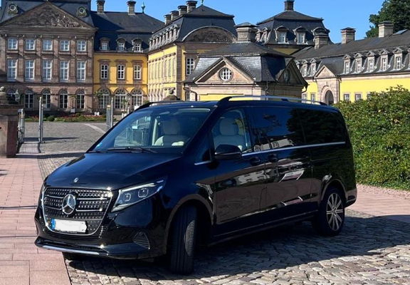 Home Ein schwarzer Mercedes V-Klasse Van vor einem barocken Schloß.